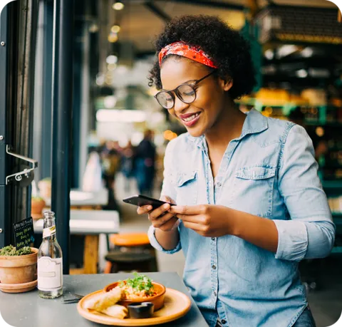 A woman smiling taking a photo of her lunch on her phone