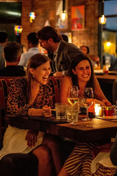 two women laughing over dinner and glasses of wine